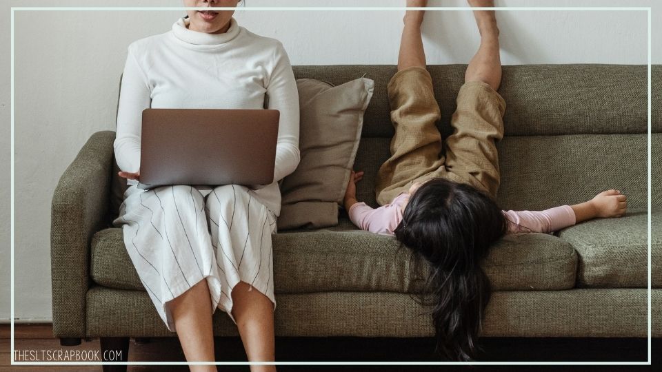 Picture of a mother on a laptop while her child is sat on the sofa, upside down, next to her. Demonstrating how parents can be disengaged in parent coaching sessions.